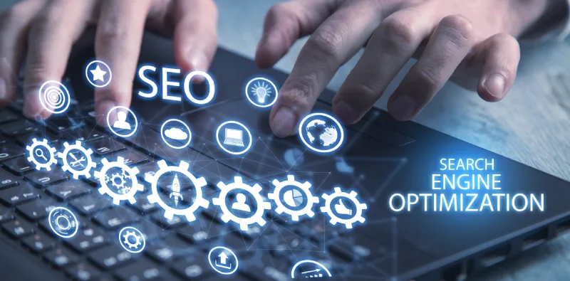 Hands typing on a laptop keyboard with digital icons representing SEO and search engine optimization emerging above the keys.